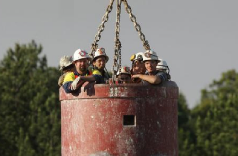 Photograph of miners in a large steel bucket known as a kibble.